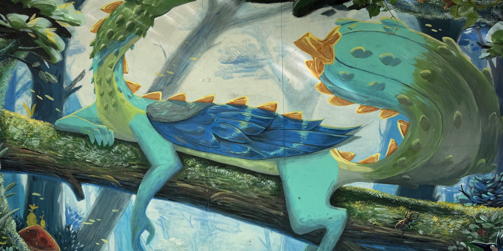 A hand-painted dragon with a blue feathered wing and orange spines, curled along a mossy branch above a pale blue forest — part of the mural covering the walls at Pickles.